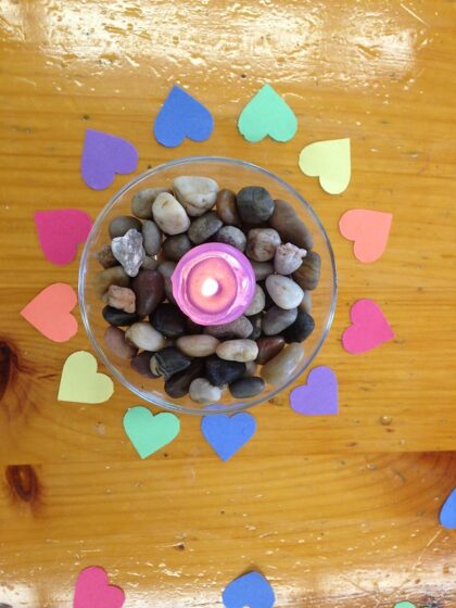 lit candle in surrounded by rocks and paper hearts in a circle